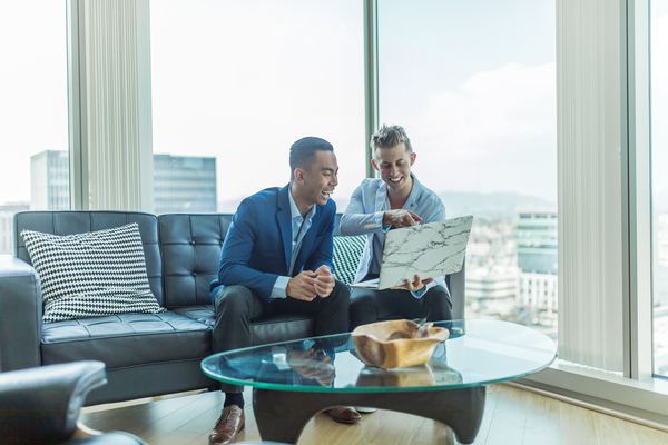 two male coworkers sitting in a private office while smiling and looking at a laptop